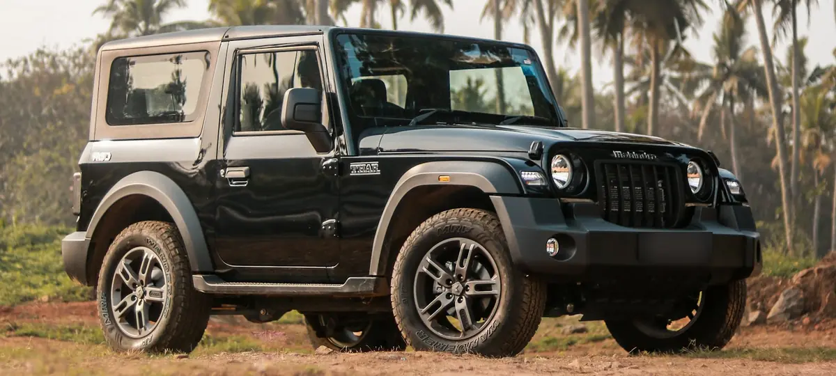 Black Mahindra Thar parked on red earth under palm trees